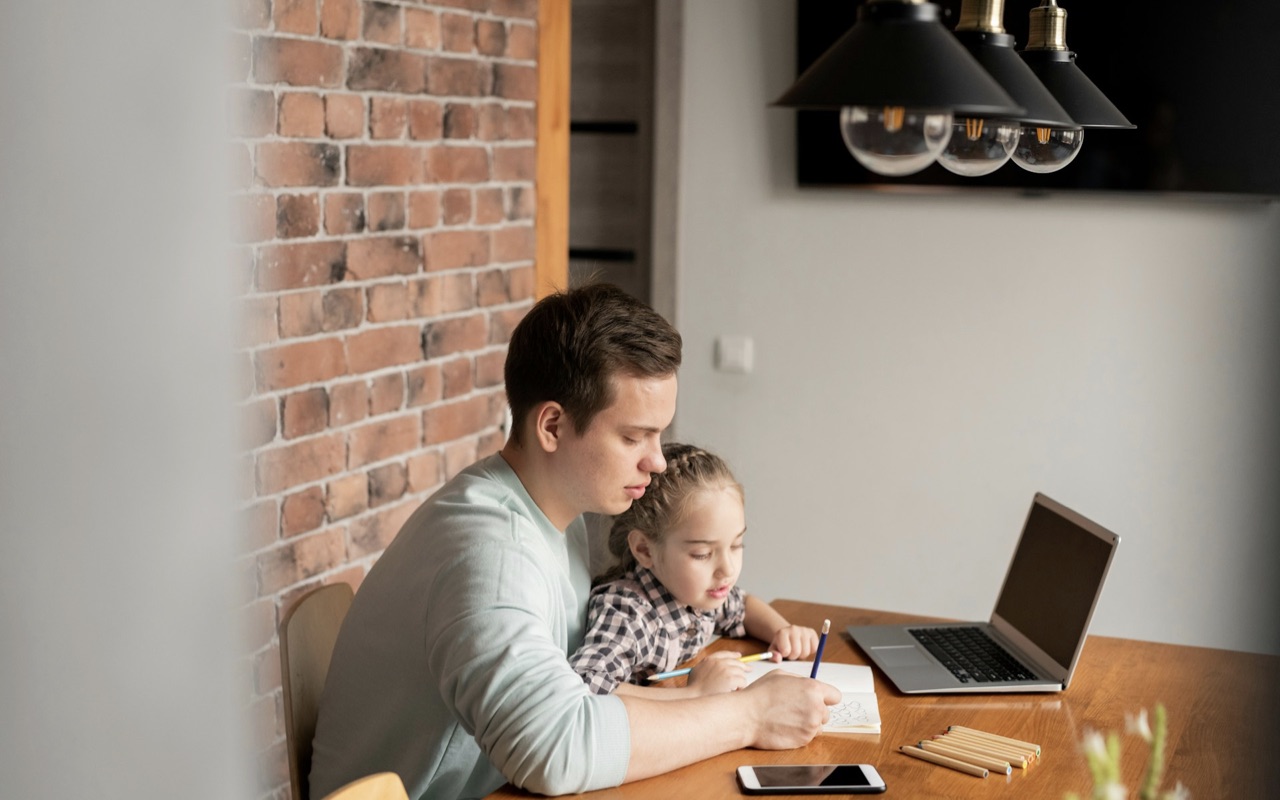 A father working from home, with his kid at the same desk